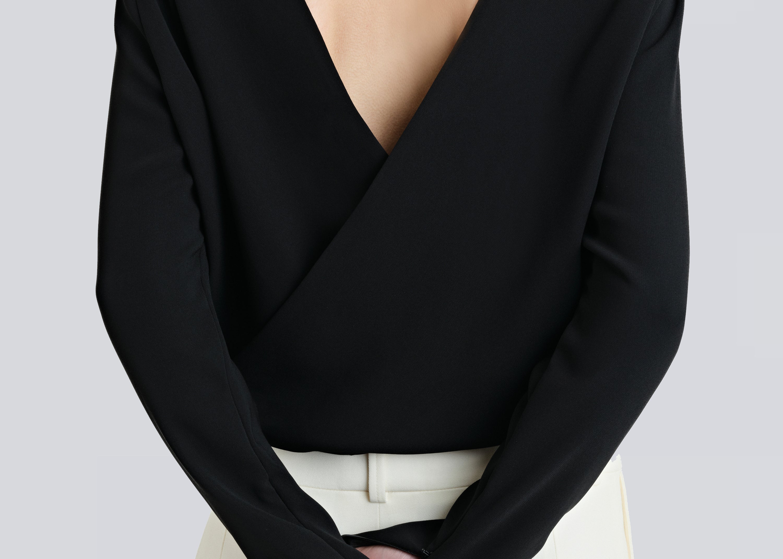A person wearing a black, backless, cross-over shirt with long sleeves and a V-neckline, by sener besim