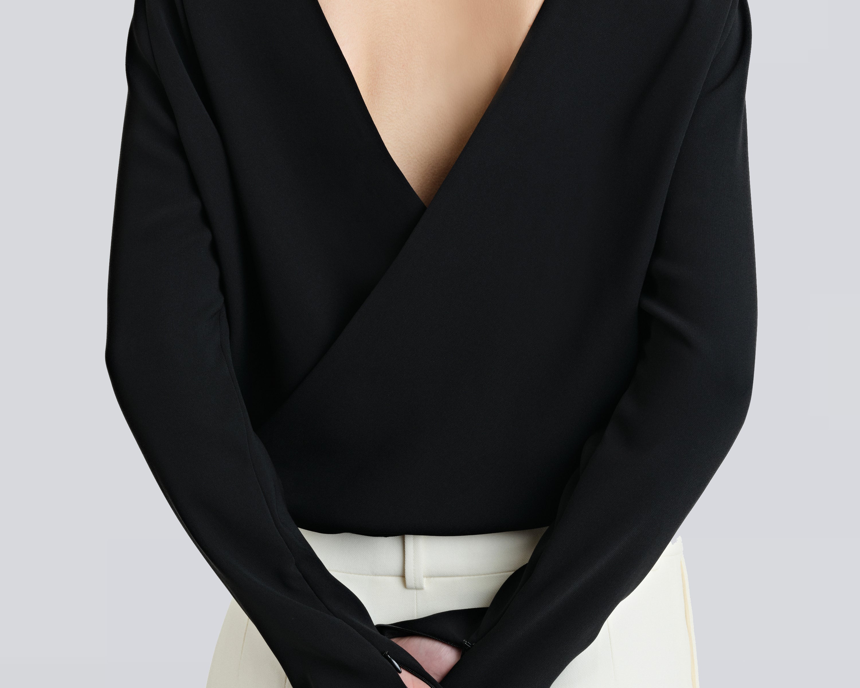 A person wearing a black, backless, cross-over shirt with long sleeves and a V-neckline, by sener besim