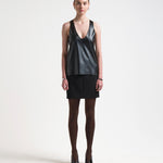 A model is wearing a black vegan leather tank top with a deep curved neckline and sleeveless design.