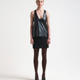 A model is wearing a black vegan leather tank top with a deep curved neckline and sleeveless design.