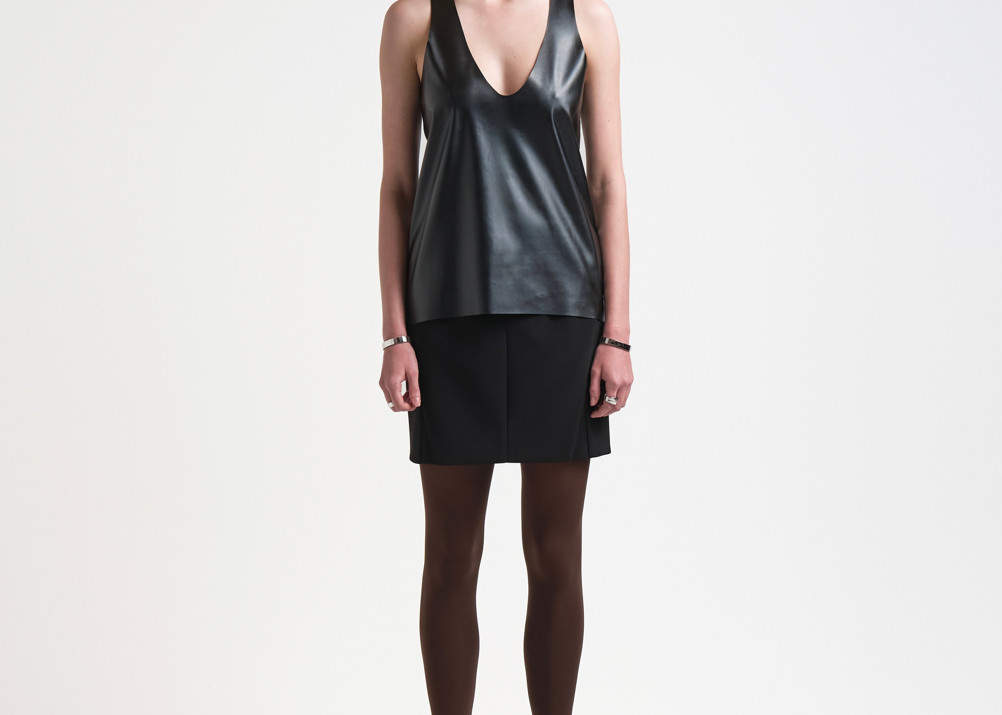 A model is wearing a black vegan leather tank top with a deep curved neckline and sleeveless design.