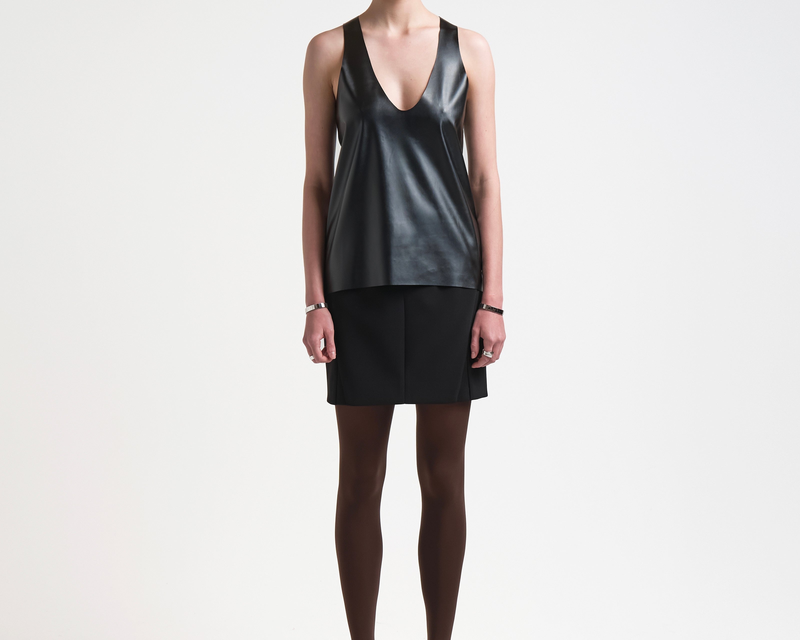 A model is wearing a black vegan leather tank top with a deep curved neckline and sleeveless design.