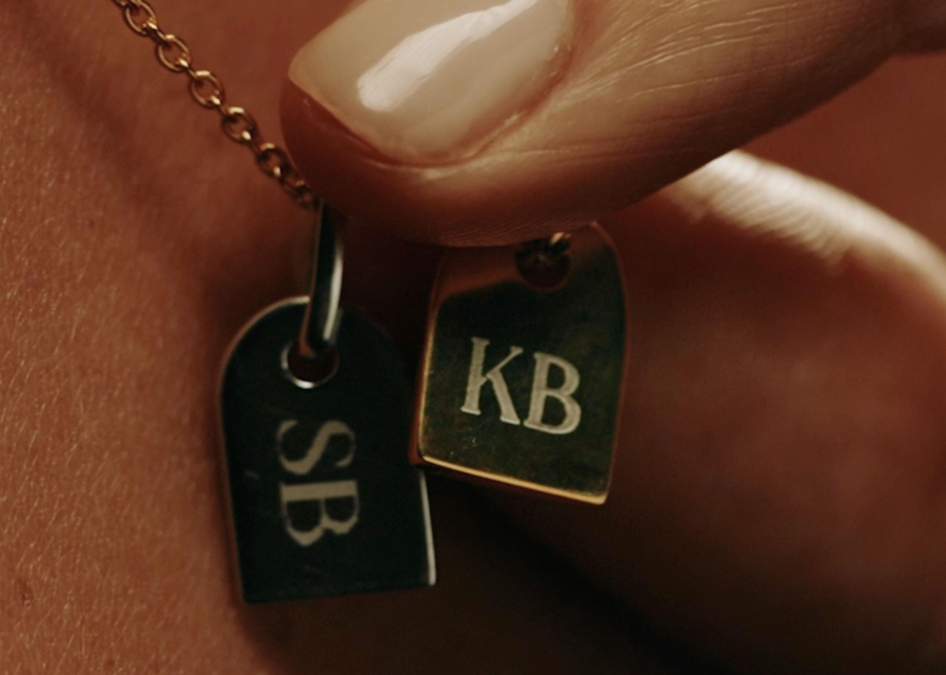 Close-up of a necklace with two pendant tags, engraved with 'SB' and the other 'KB' - Sener Besim