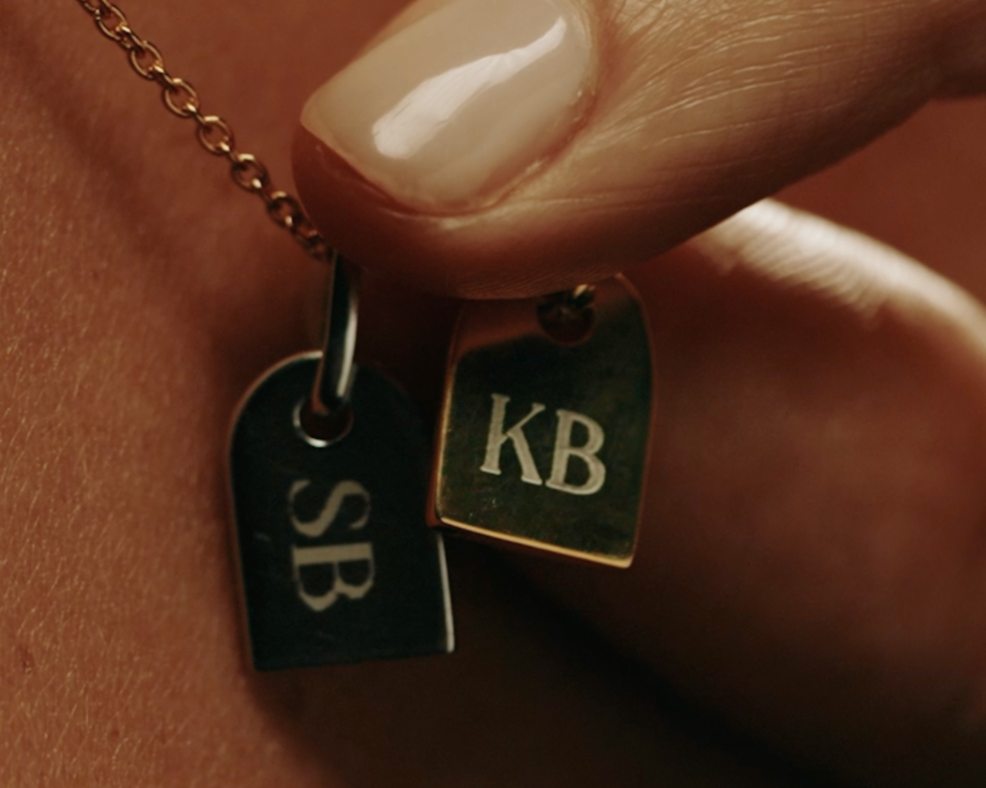Close-up of a necklace with two pendant tags, engraved with 'SB' and the other 'KB' - Sener Besim
