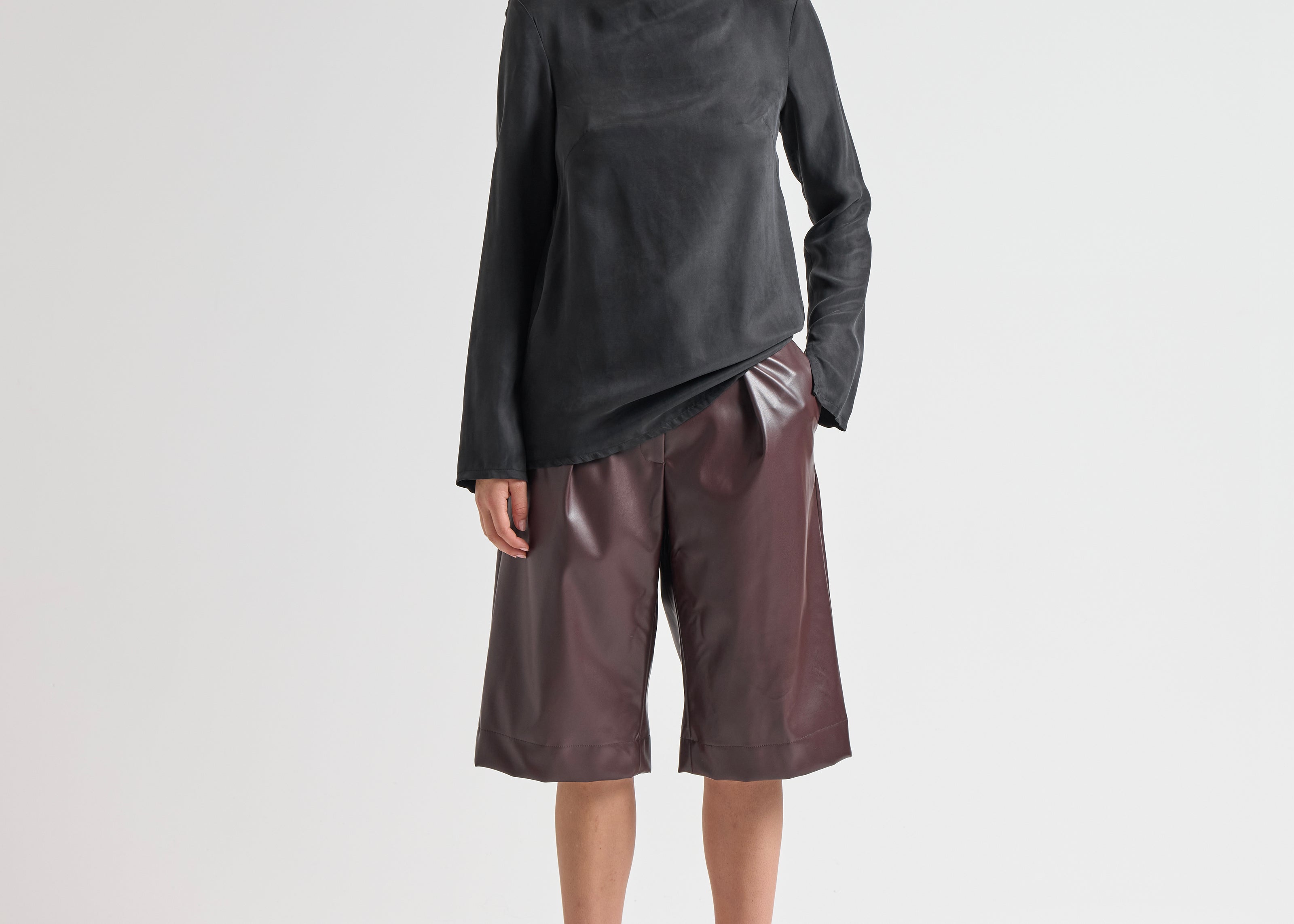 Woman wearing a black turtleneck and brown leather shorts on a white background by sener besim