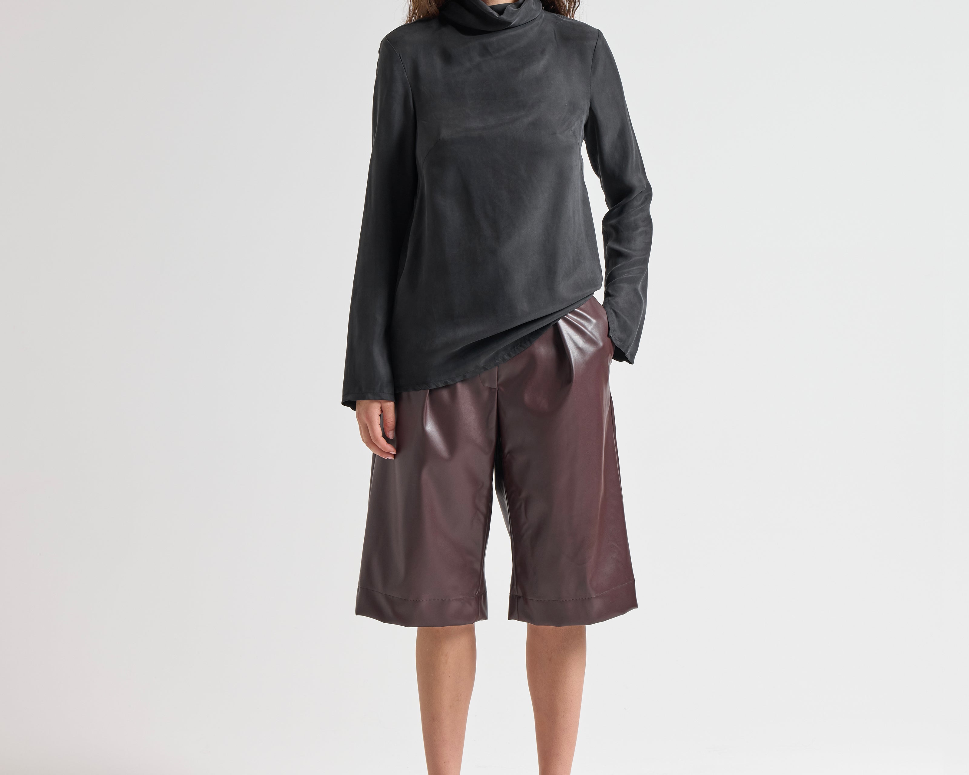 Woman wearing a black turtleneck and brown leather shorts on a white background by sener besim