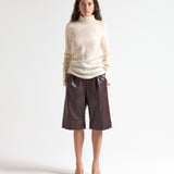 Woman wearing a beige blouse and brown leather shorts on a white background by sener besim