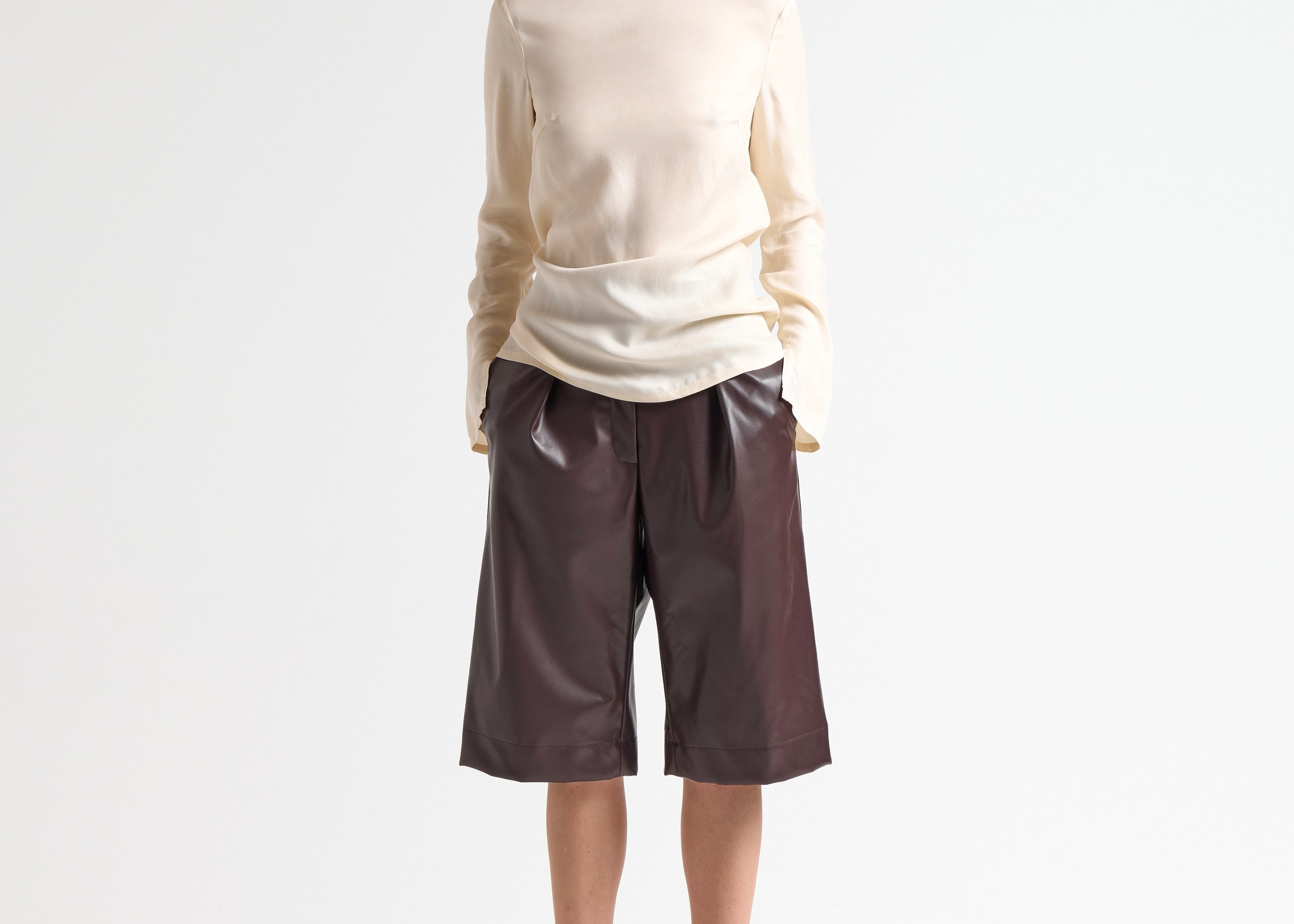 Woman wearing a beige blouse and brown leather shorts on a white background by sener besim