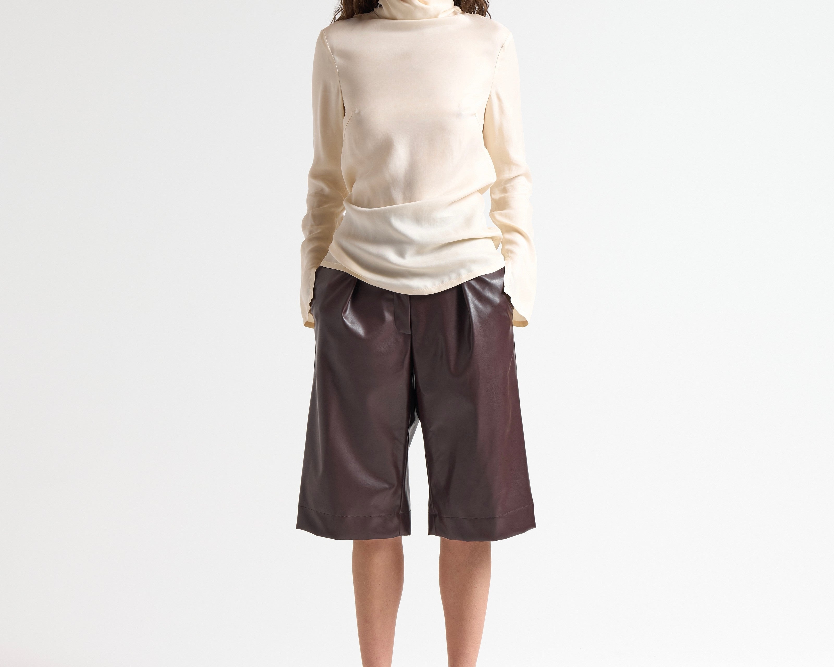 Woman wearing a beige blouse and brown leather shorts on a white background by sener besim