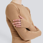 A person wearing a beige Merino Thumbhole Crewneck sweater with thumbhole cuff detail