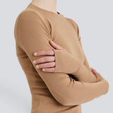 A person wearing a beige Merino Thumbhole Crewneck sweater with thumbhole cuff detail