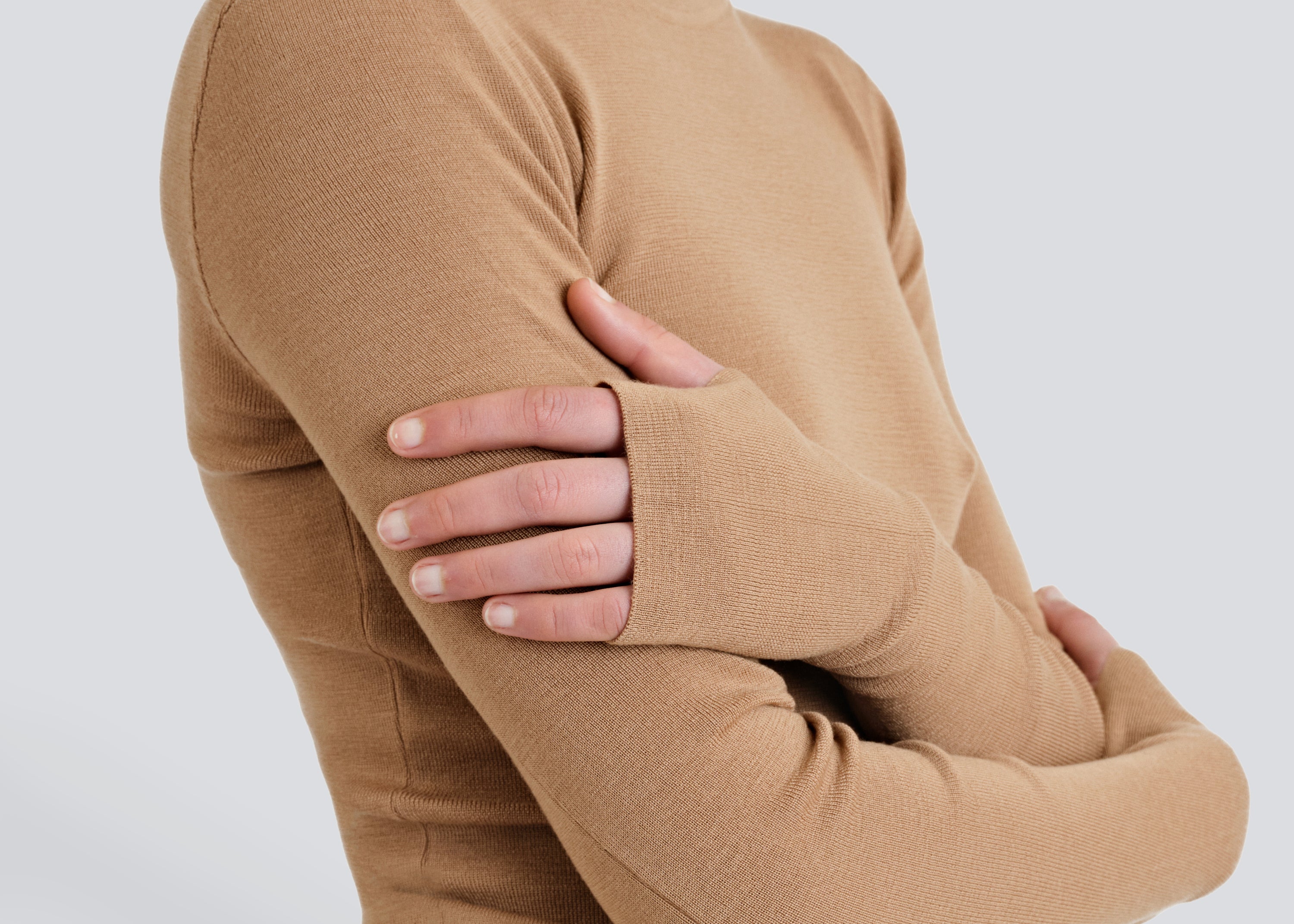 A person wearing a beige Merino Thumbhole Crewneck sweater with thumbhole cuff detail