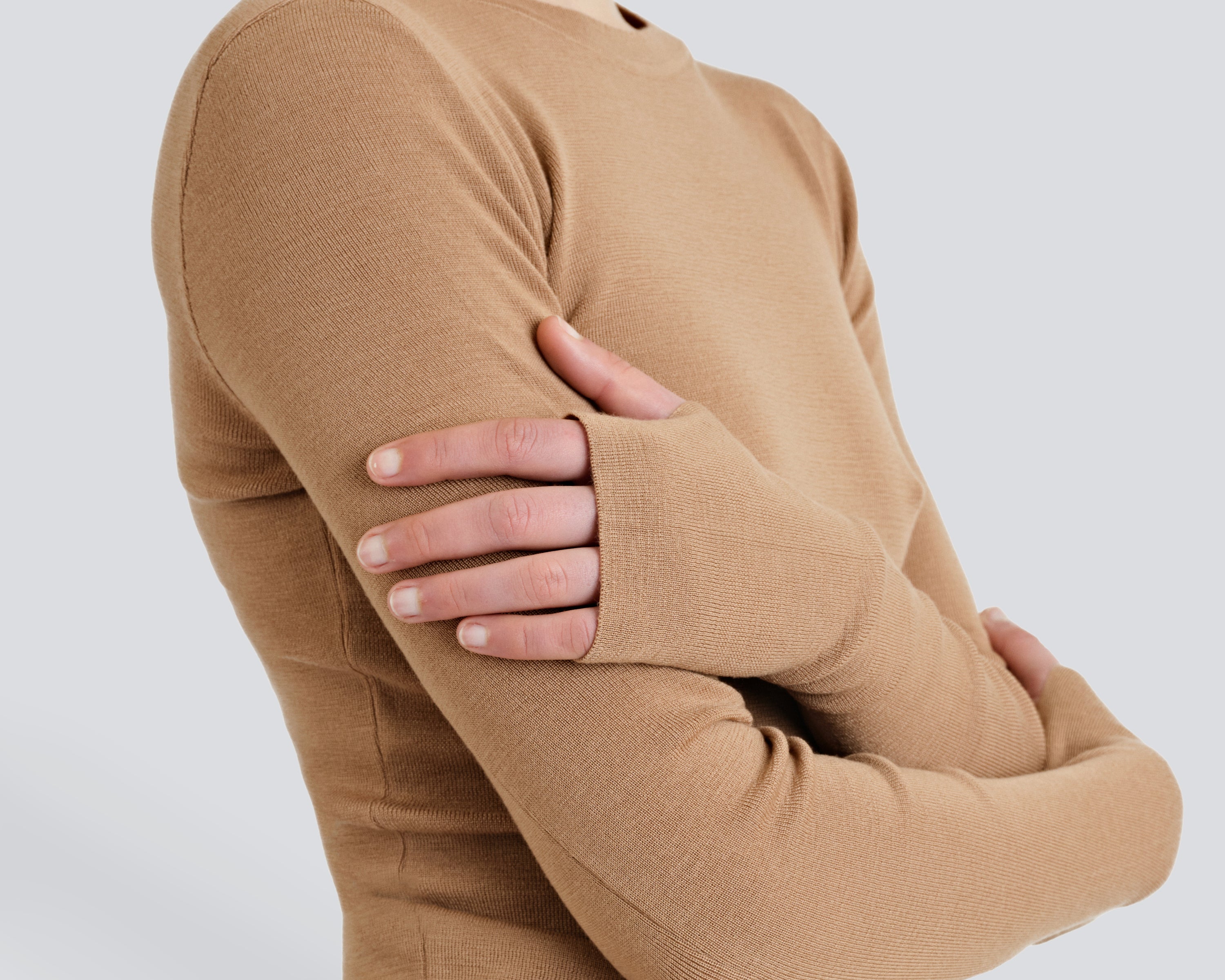 A person wearing a beige Merino Thumbhole Crewneck sweater with thumbhole cuff detail