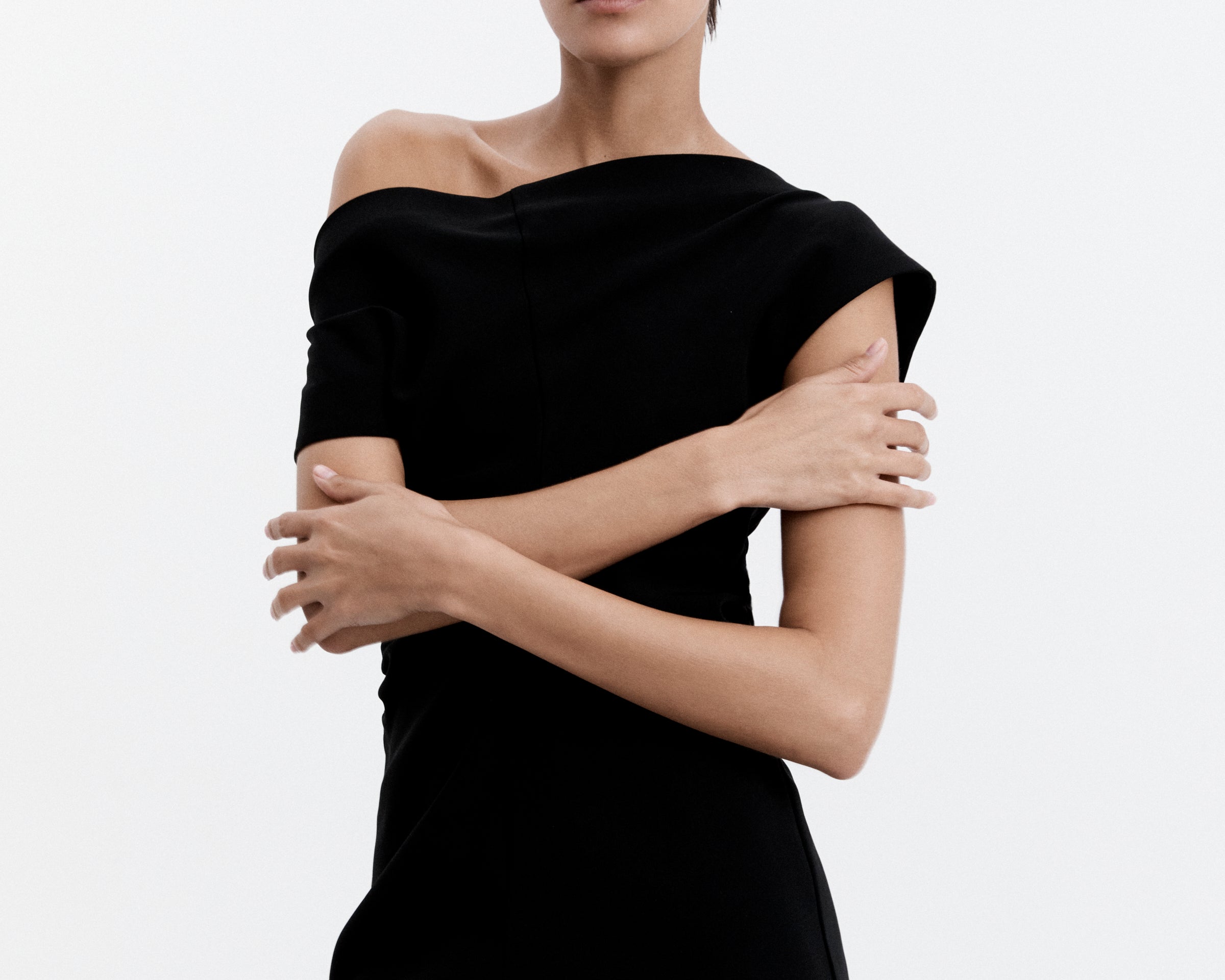 A model wearing a black mini dress with a high, structured neckline, cap sleeves, side ruching, and an exposed zipper at the back.