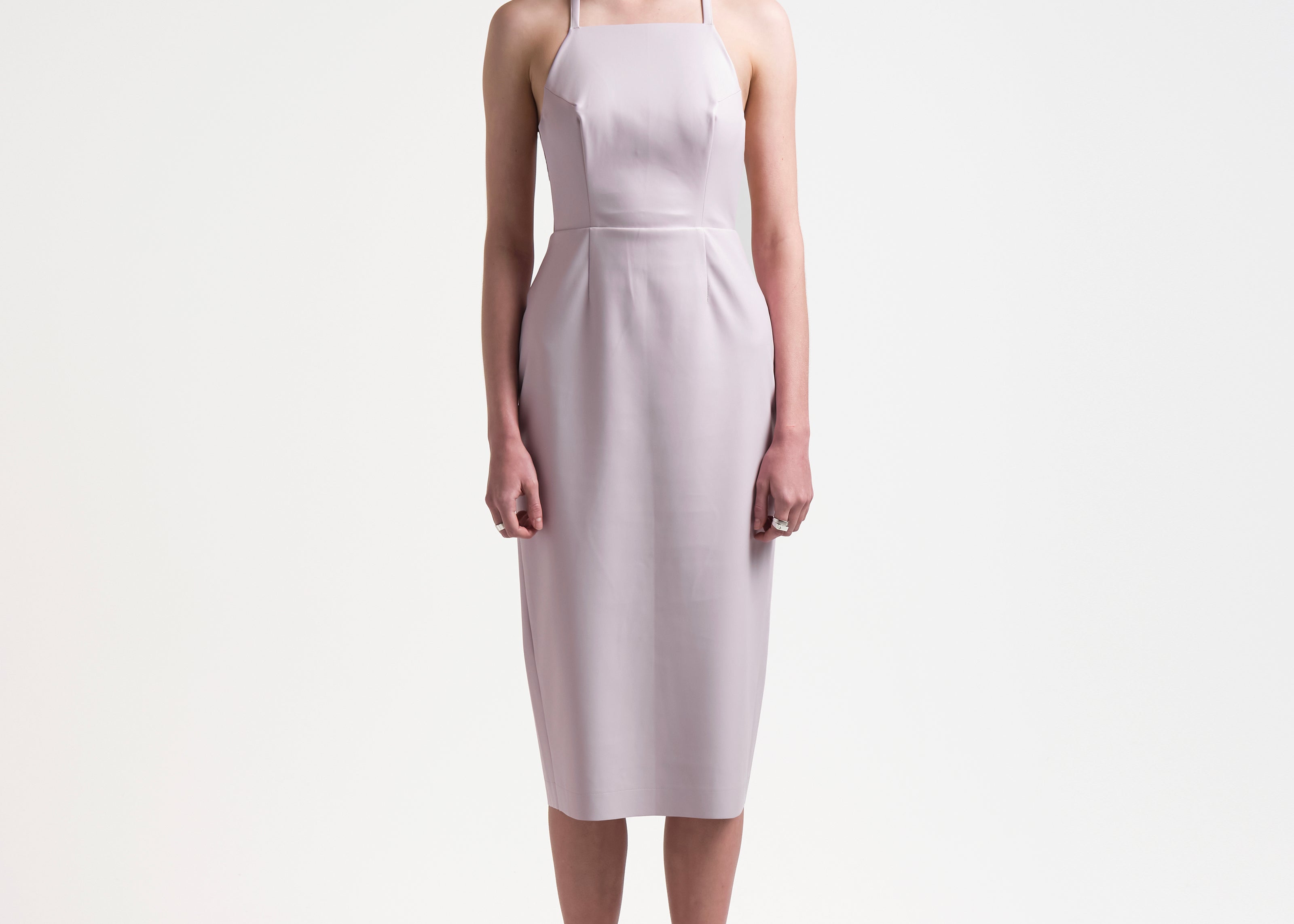 model wearing a pale pink sleeveless dress with an apron-front silhouette and an open back with two sets of ties by sener besim
