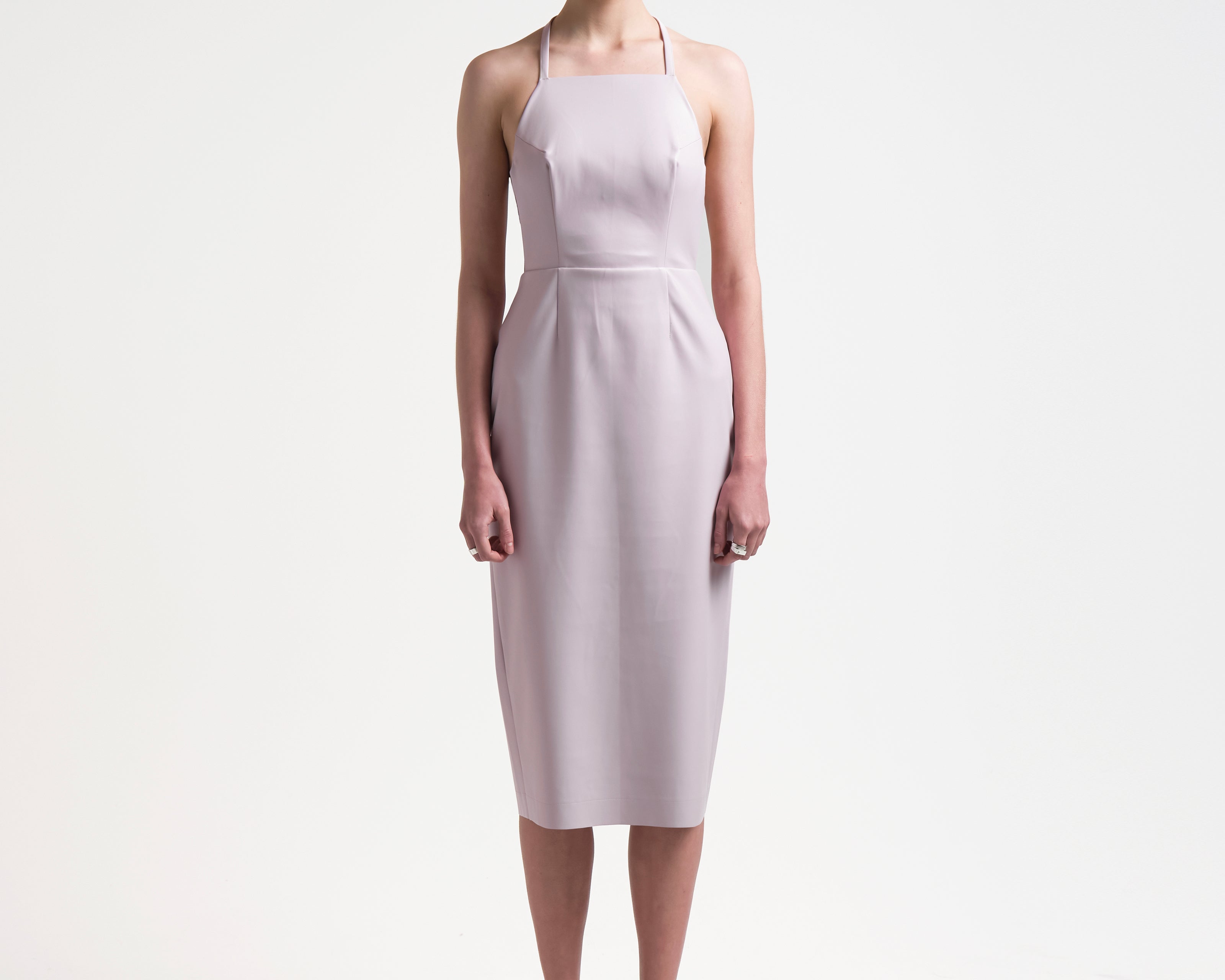model wearing a pale pink sleeveless dress with an apron-front silhouette and an open back with two sets of ties by sener besim