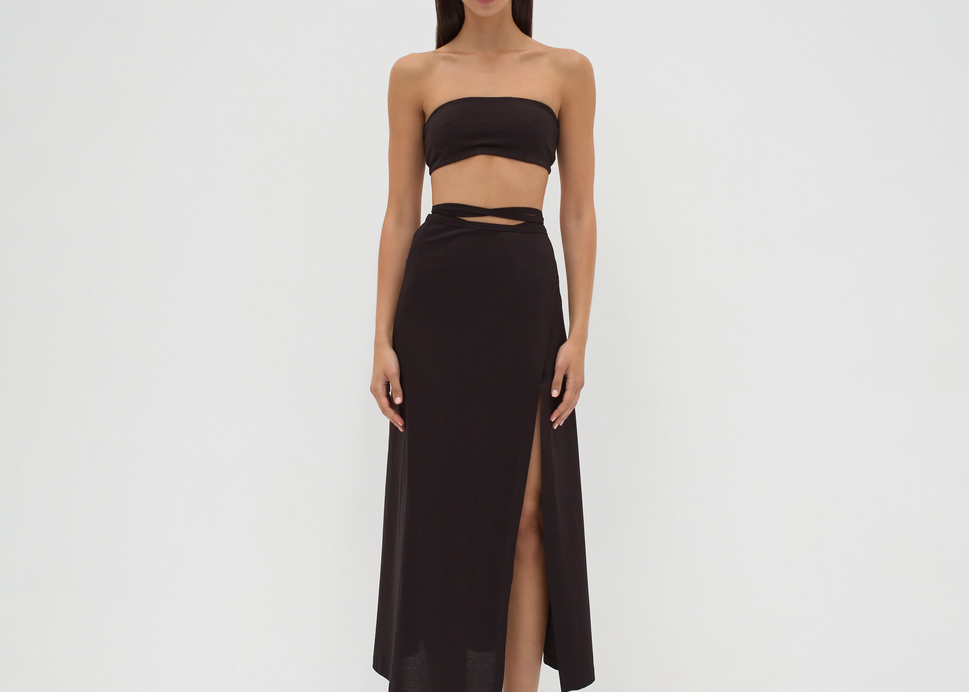 A model wearing a midi-length black skirt with extra-long ties and a split detail at the mid-thigh. The skirt is made from mercerised Turkish cotton by sener besim