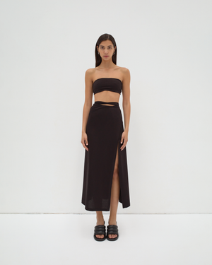A model wearing a midi-length black skirt with extra-long ties and a split detail at the mid-thigh. The skirt is made from mercerised Turkish cotton by sener besim