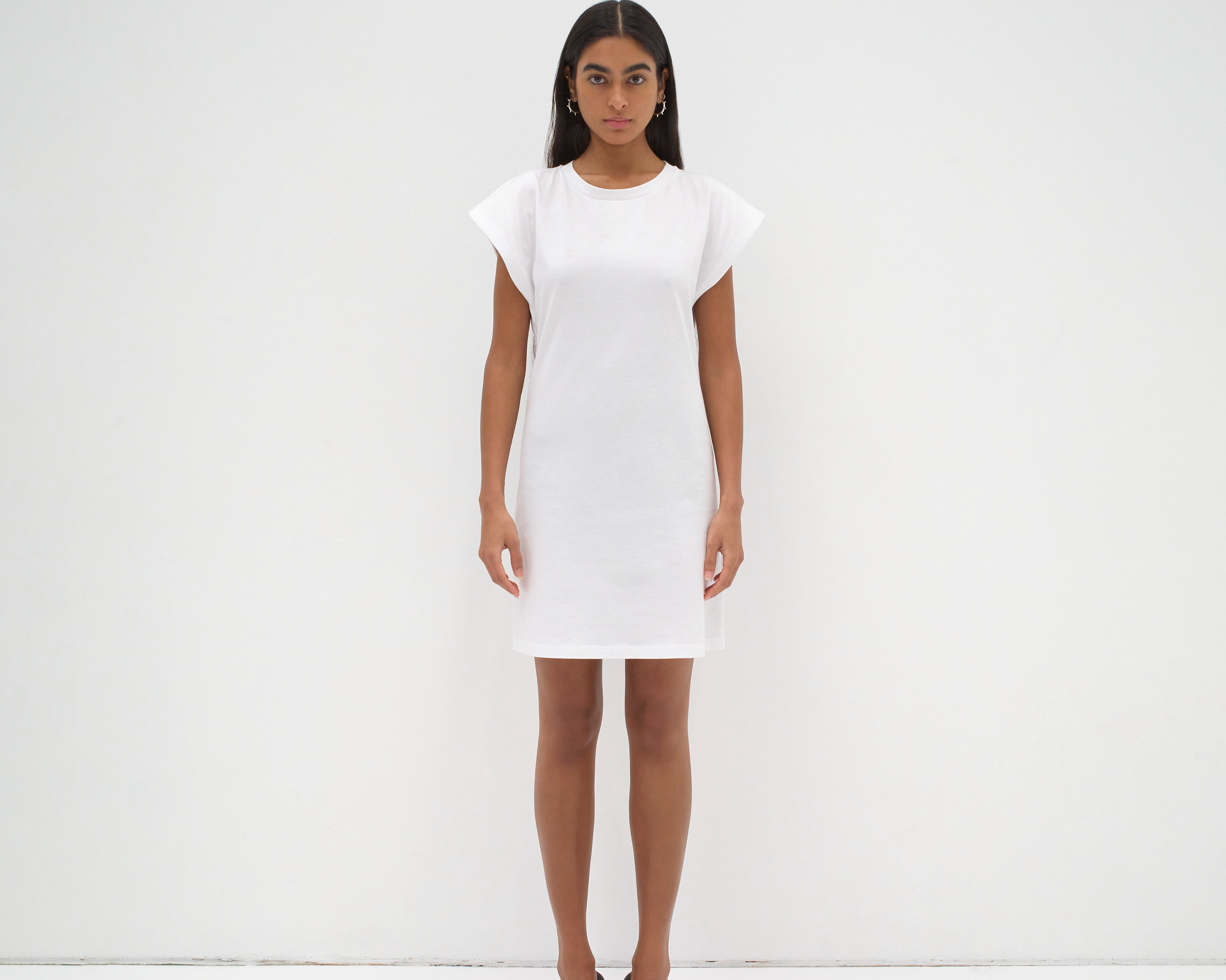model wearing a white mini dress with an open back detail and cap sleeve by sener besim