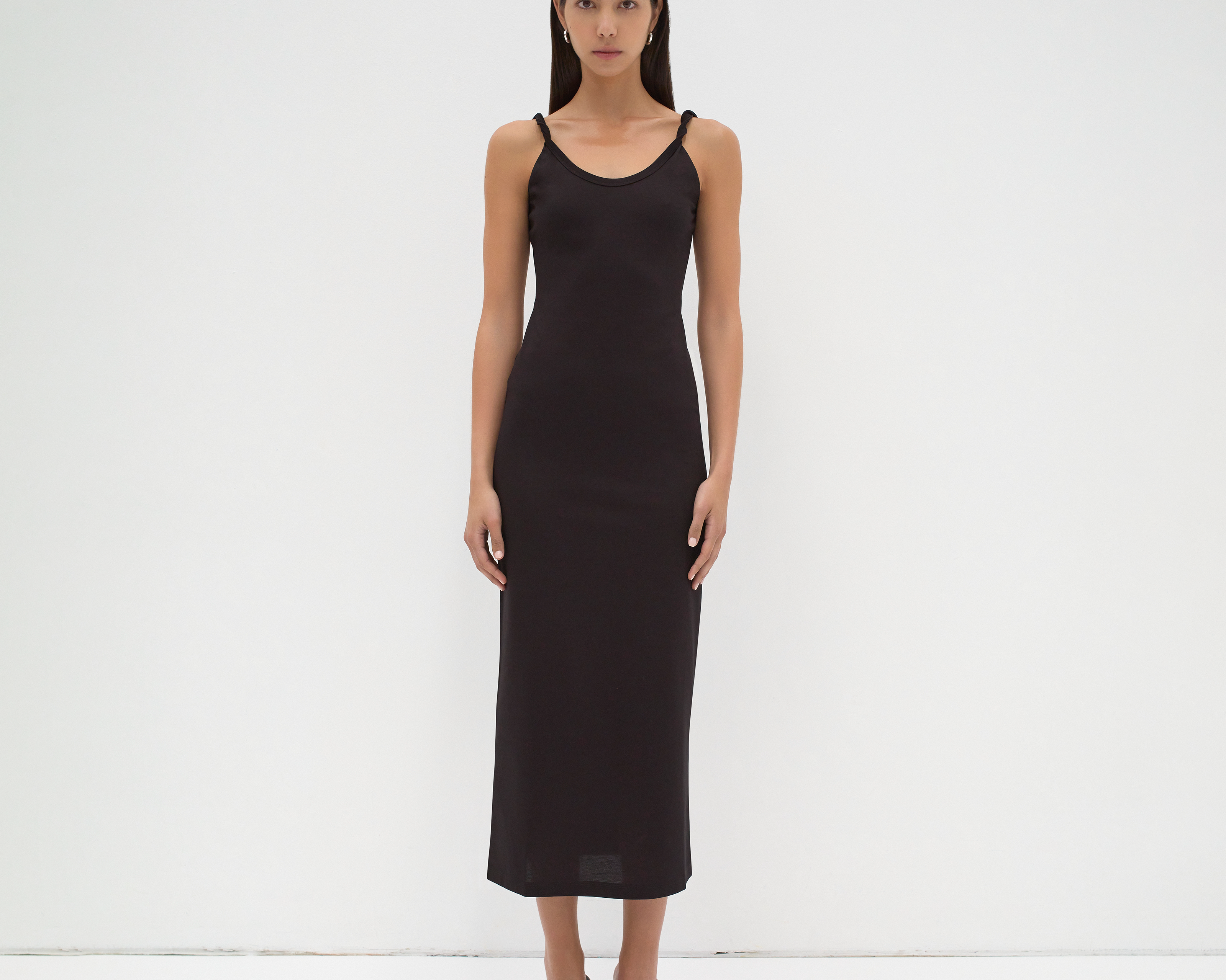 A model wearing a mid-calf length black dress with twisted strap features by sener besim