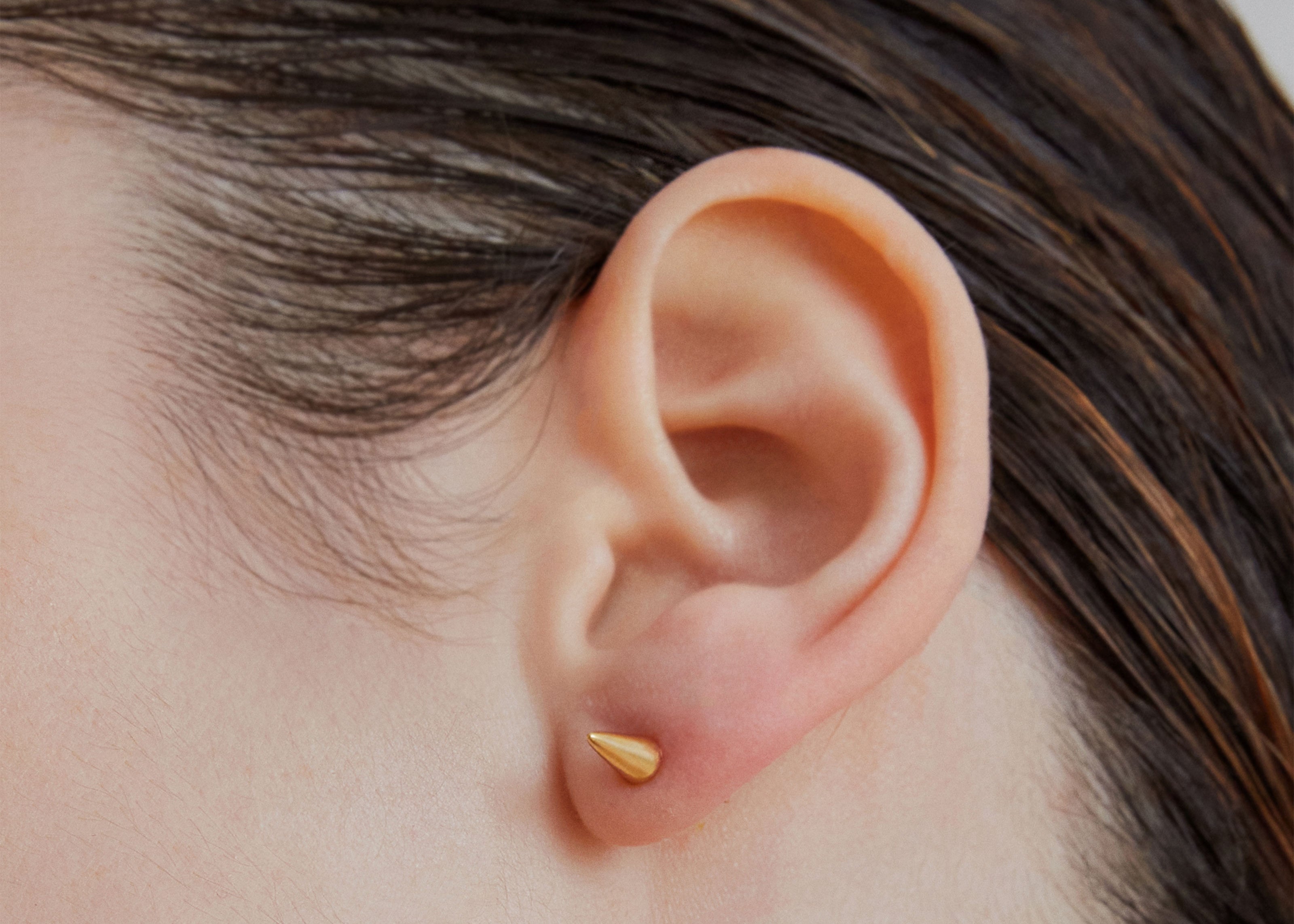 Single point spike stud earrings in gold worn on ear — Şener Besim