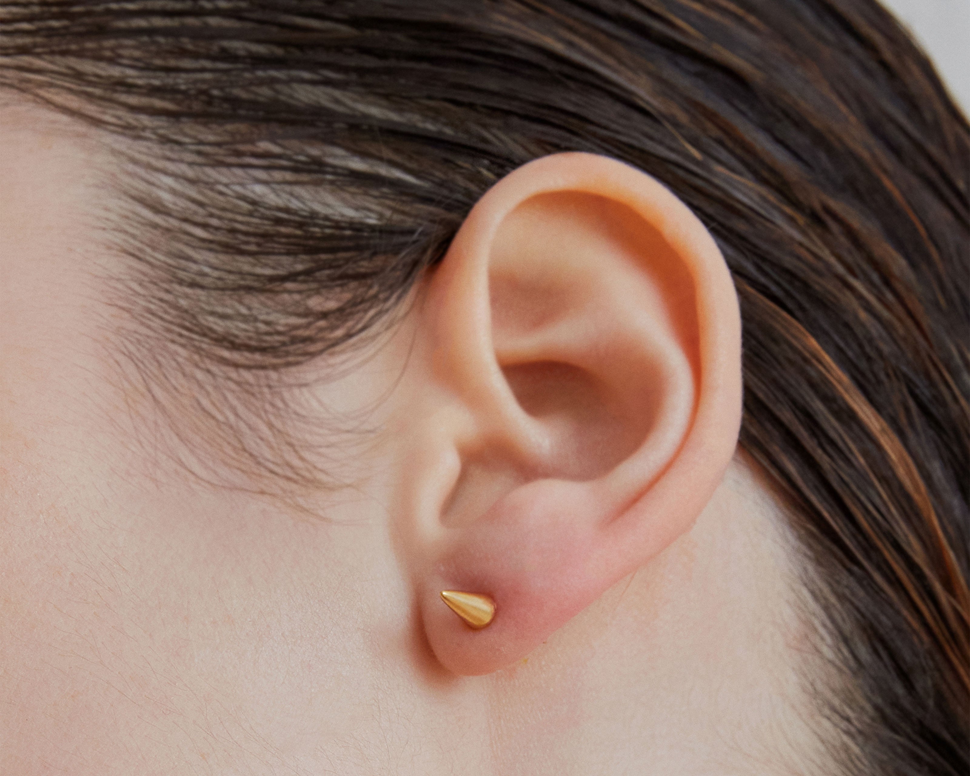 Single point spike stud earrings in gold worn on ear — Şener Besim
